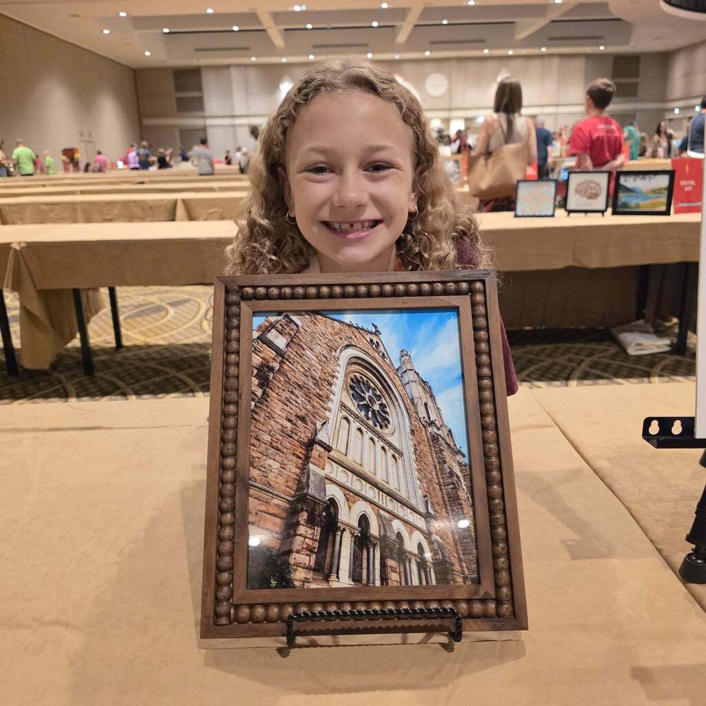 A young girl smiles at a framed picture of a church displayed on a table at an event.