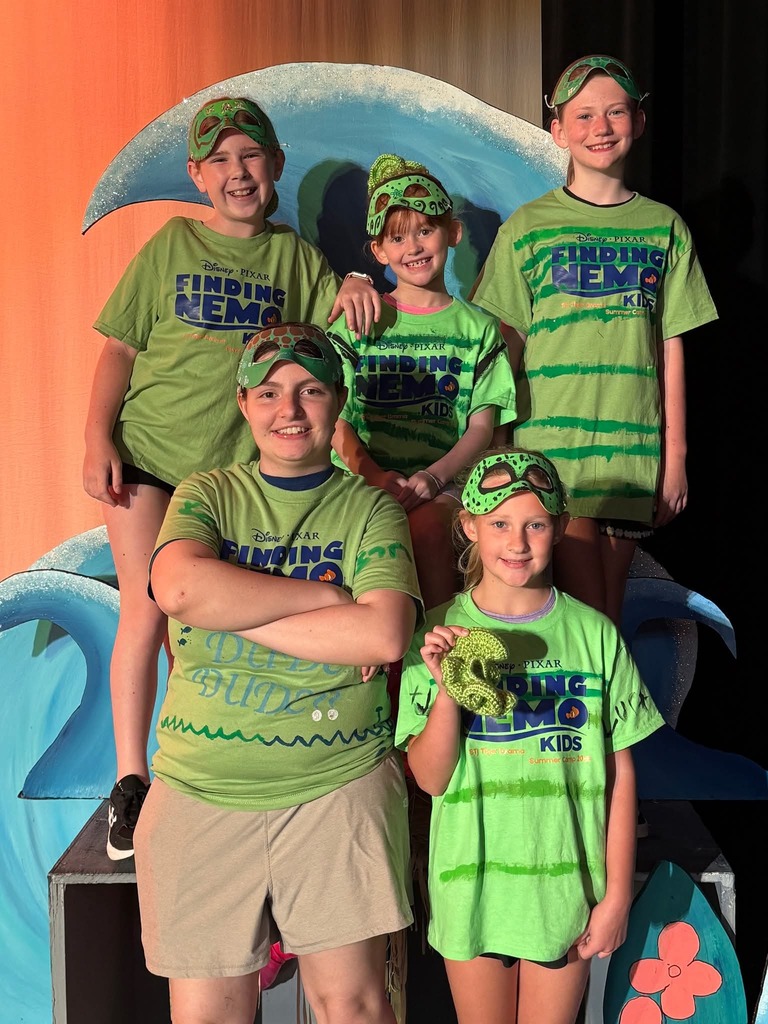 Five children in green Finding Nemo T-shirts pose on a stage with a wavy blue backdrop.