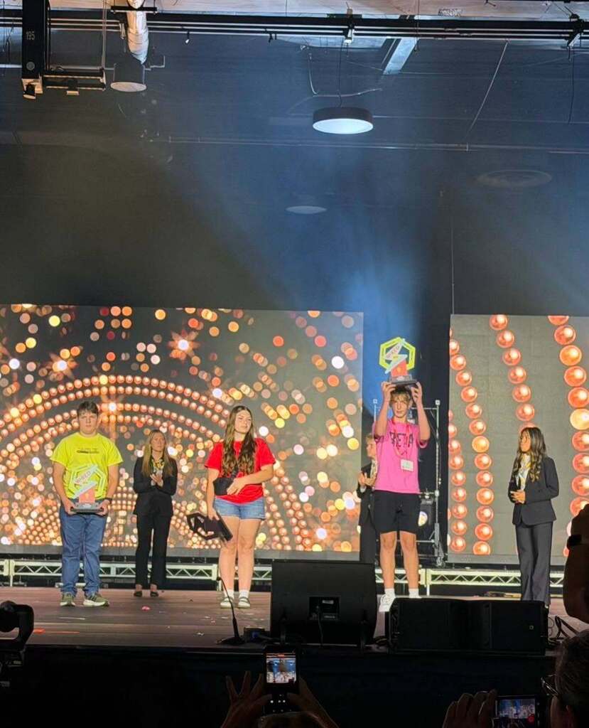 People on stage, with a large screen behind them showing circular patterns. A spotlight illuminates the center.