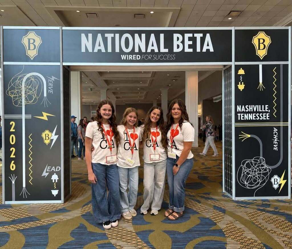 Four women stand in front of a sign that reads "National Beta" and "Nashville, Tennessee." They wear white shirts.