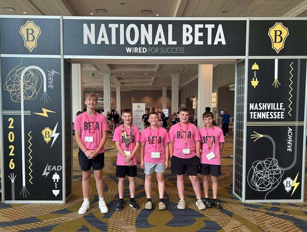 Five young boys in pink shirts and black shorts pose at a booth reading "National Beta" at a convention.