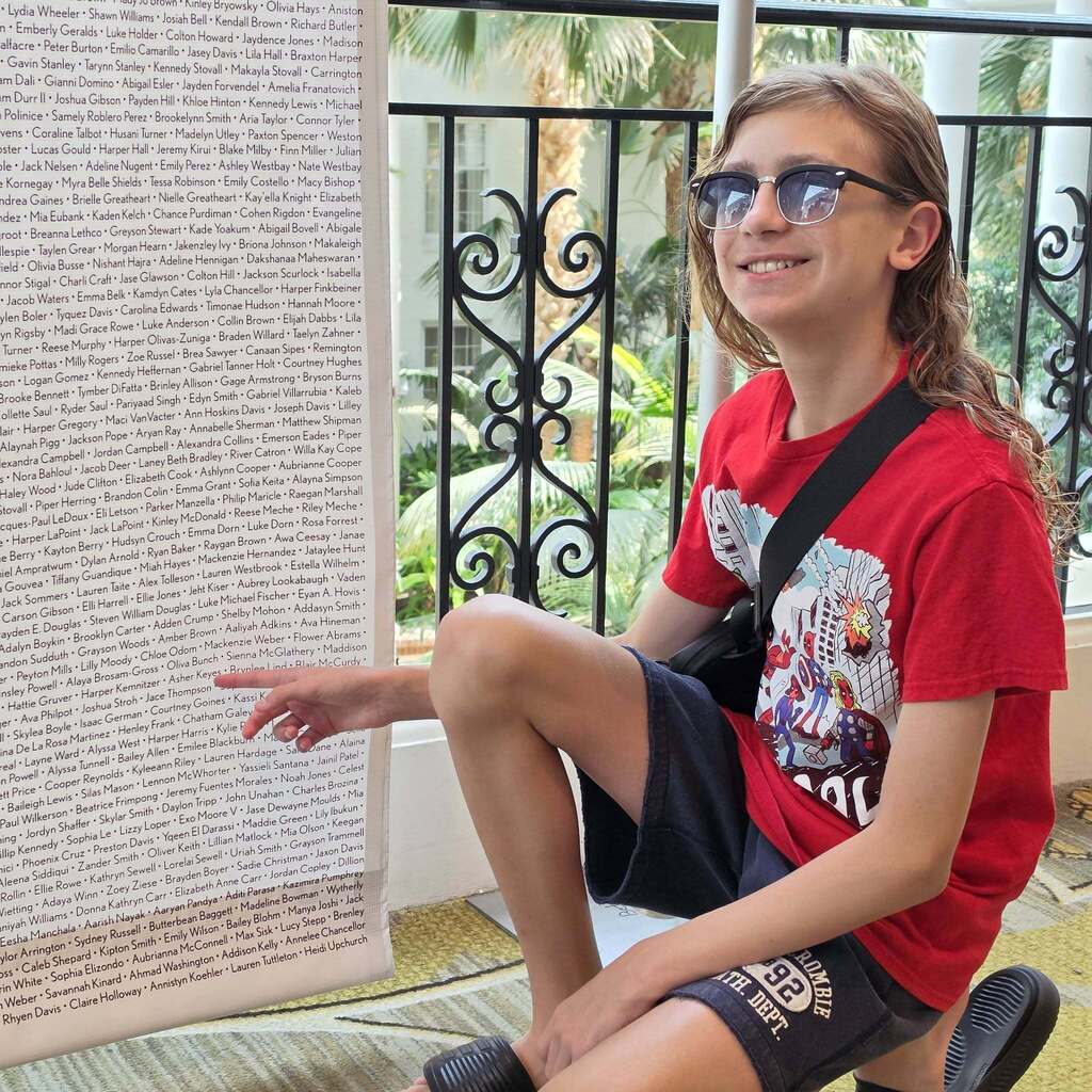 A person in a red shirt with a printed design sits on a bench with a wall in the background.