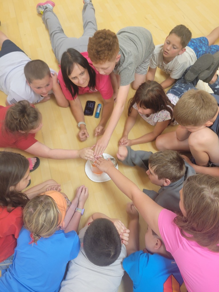Group of children and adults sitting in a circle on a wooden floor, holding hands.