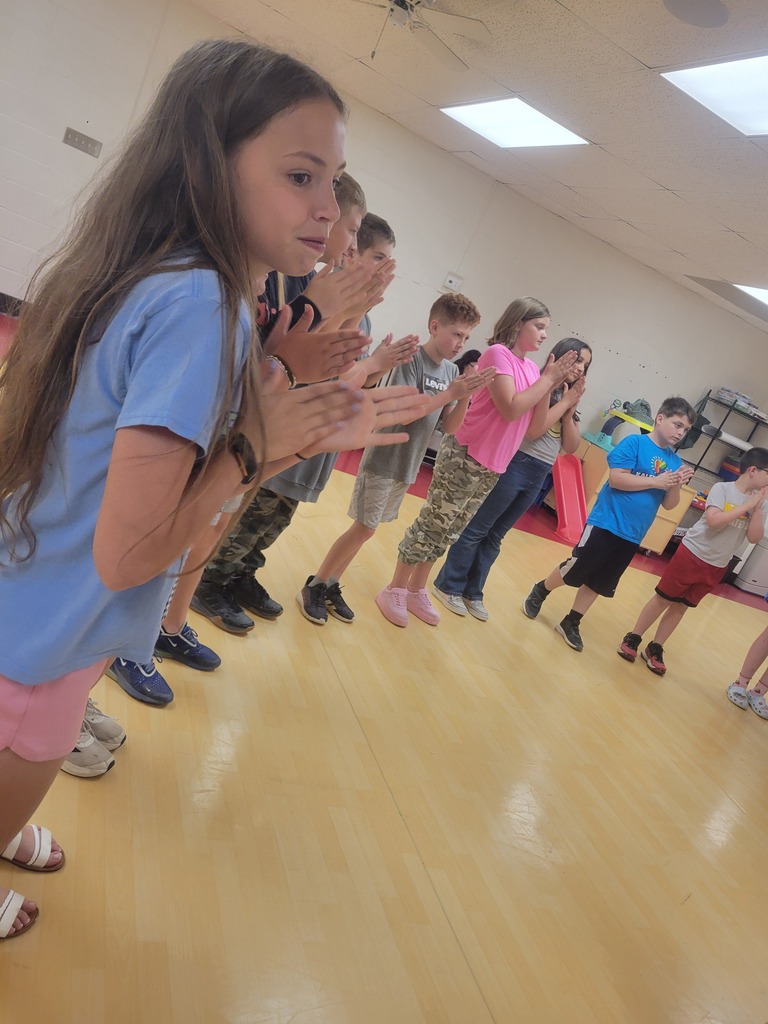 A group of children and a young girl clapping hands, standing on a wooden floor.