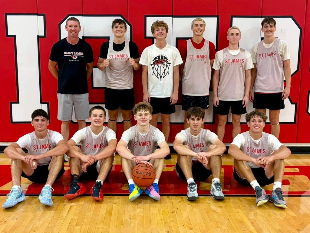 A group of young basketball players posing for a team photo on a wooden court. They wear matching shirts and shorts.