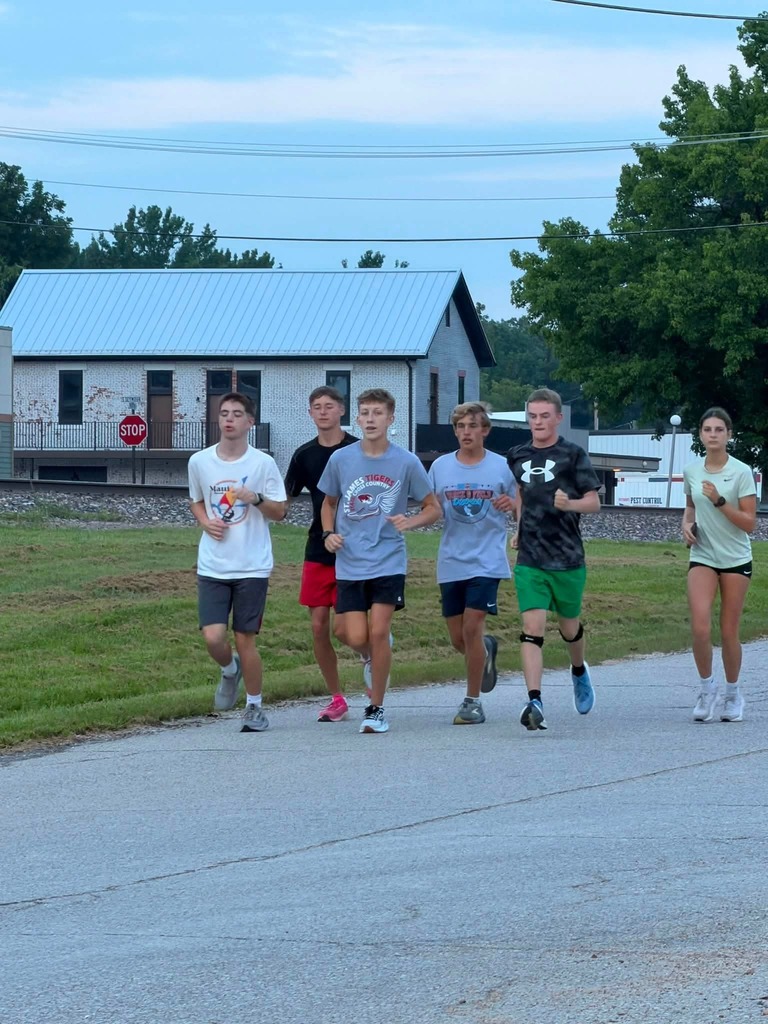 Five young people jogging on a road. One is in a white shirt, two are in gray. Two are in black.