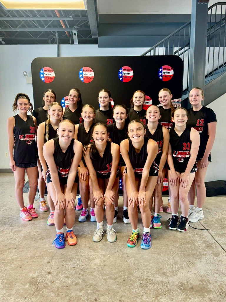 A group of girls wearing identical black uniforms pose for a photo in a room with stairs.