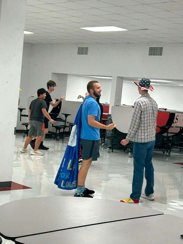 Several people in an open office space, with one person wearing a blue cape.