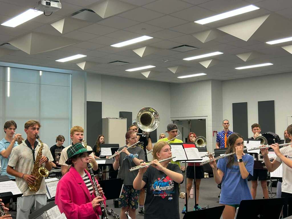 A group of students in a music room, practicing with various instruments such as saxophones, trumpets, and flutes.