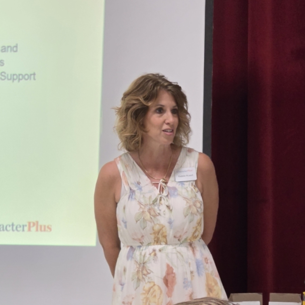 Woman in a sleeveless floral dress stands next to a projector screen displaying text.