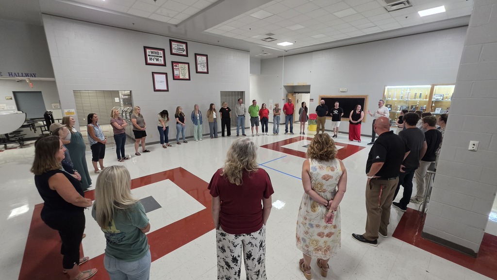 Group of people standing in a large, open room with white walls and red floor markings.