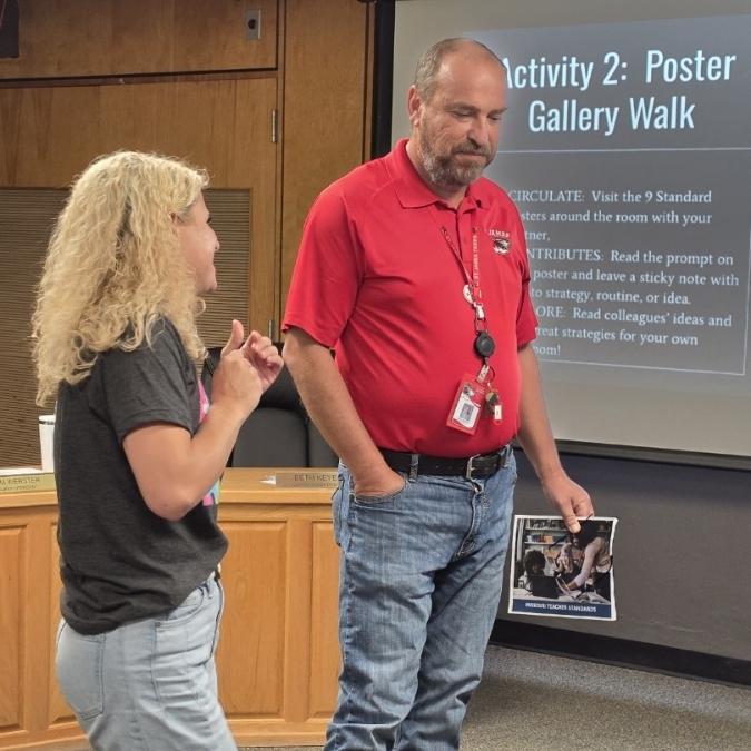 Man and woman stand in front of presentation screen, man in red shirt, woman in gray shirt.