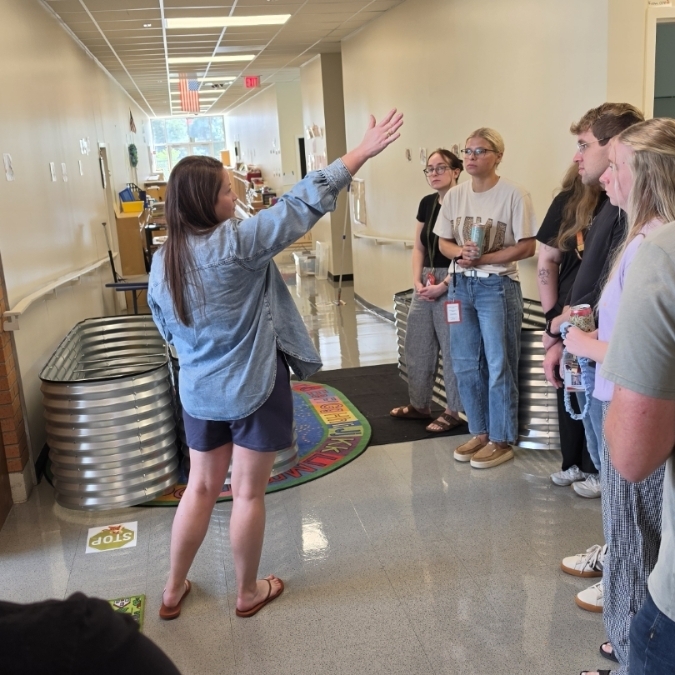 A hallway with metal containers, a carpet, and people. A woman raises her hand.