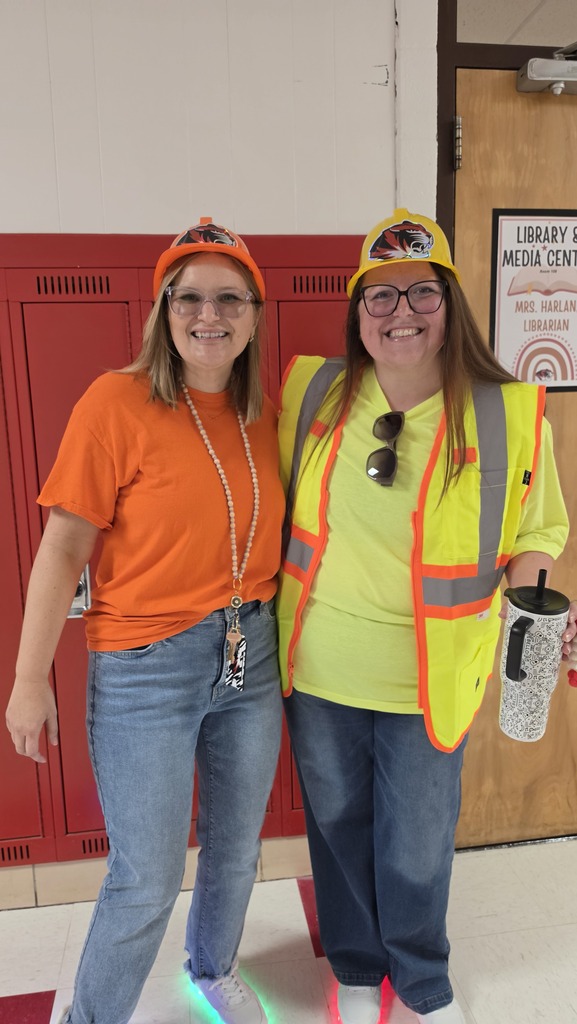 Two women stand together wearing hard hats and construction vests. 