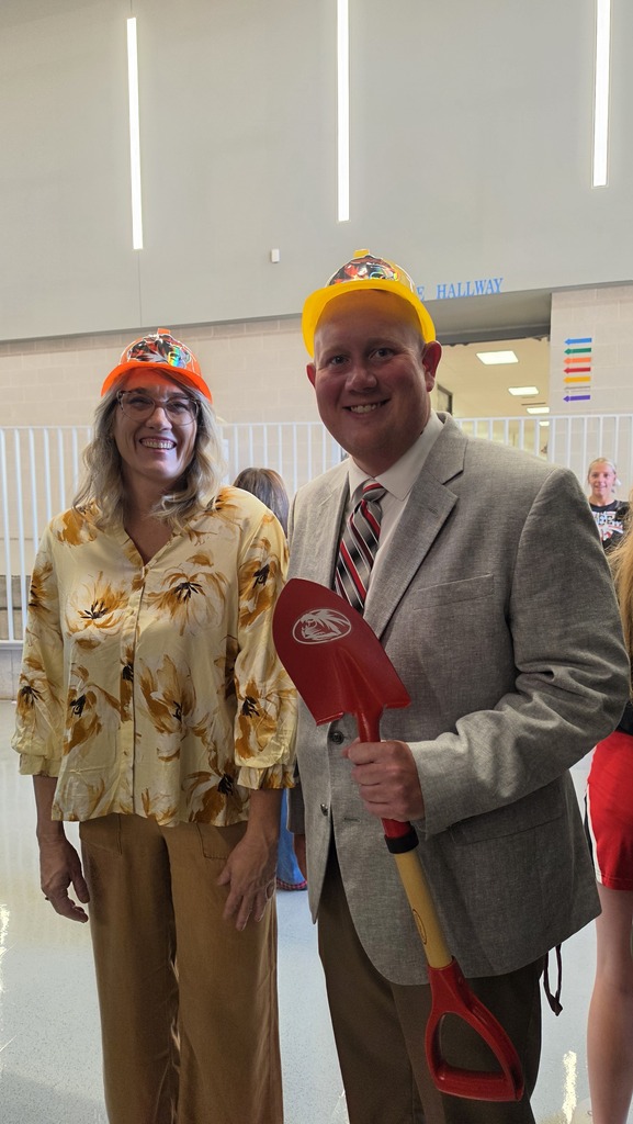 Man and woman stand with hard hats on. 