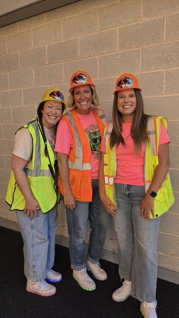Three women stand together wearing hard hats and construction vests. 