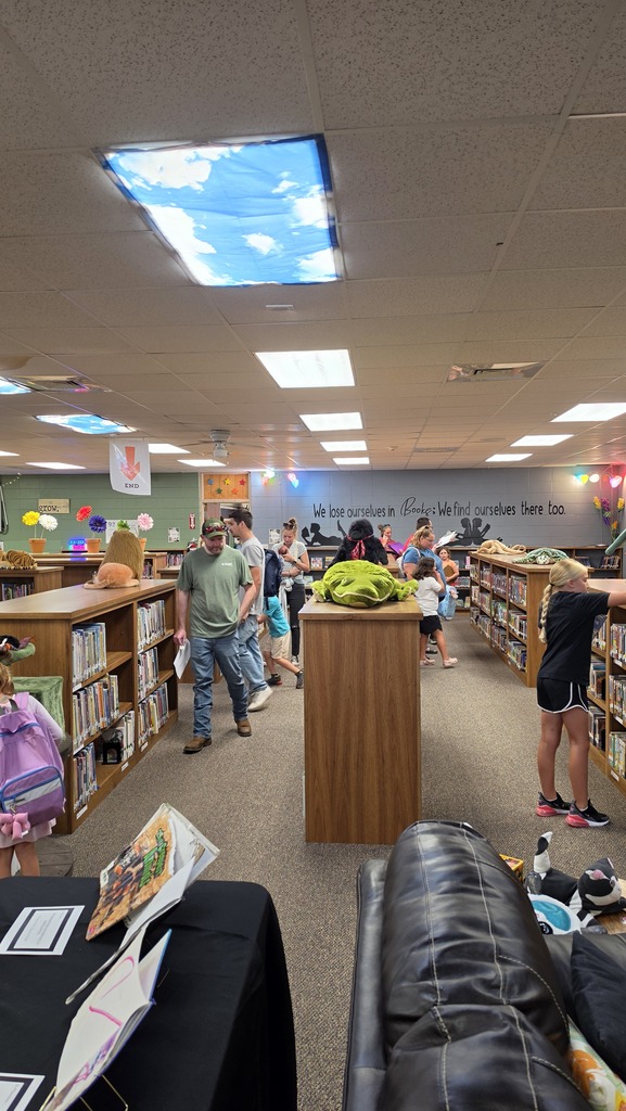 Interior of a library with tables and people; shelves of books, ceiling lights, and a skylight in the background.