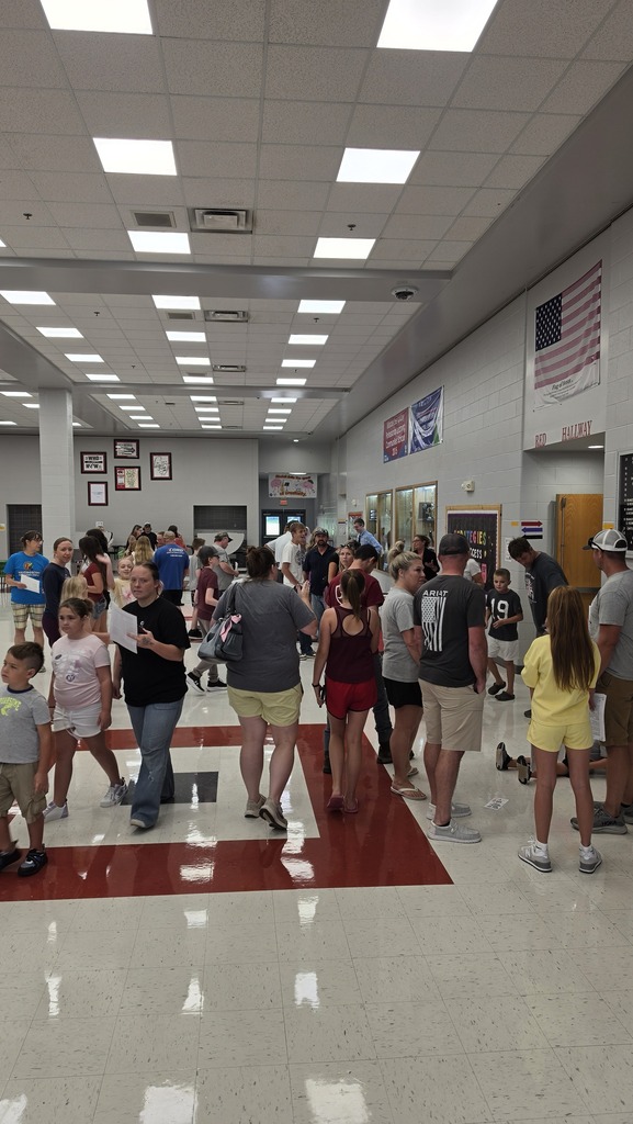 Hallway filled with people, some walking, others standing. Red floor, white walls, and overhead lights.
