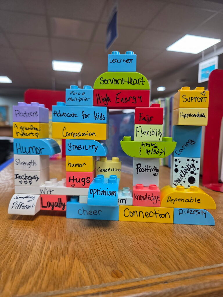 Display of colorful Lego blocks with written traits like "Flexibility," "Advocate for Kids," and "Diversity" on a wooden table.