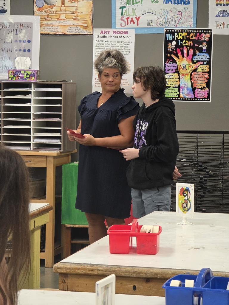 A woman in a dark blue dress stands next to a boy in a black hoodie. They are looking at something.
