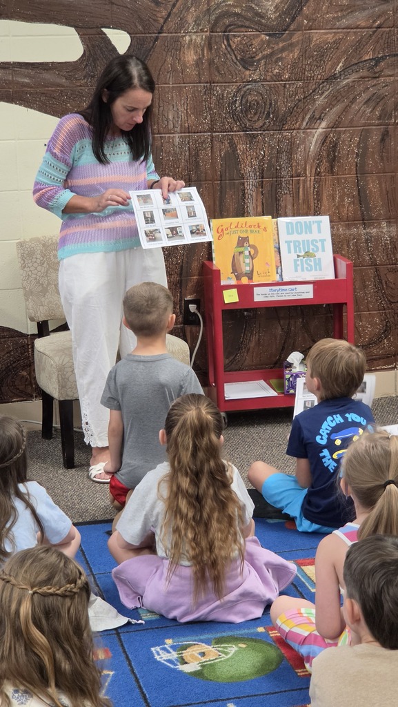 A woman reads to a group of children in a classroom. Children sit in a circle.