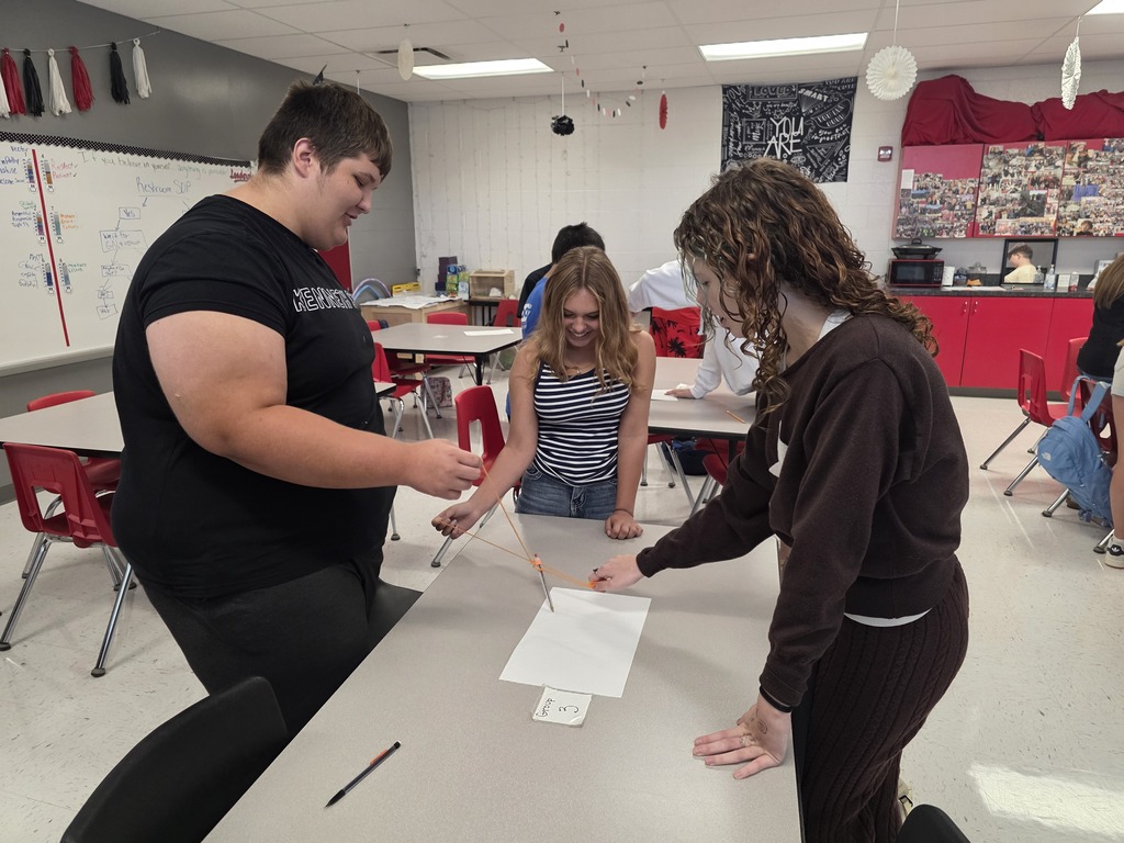 Team building in Mrs. Mulhall's class! Multiple students are working together to draw on a piece of paper with a single writing utensil and string. 