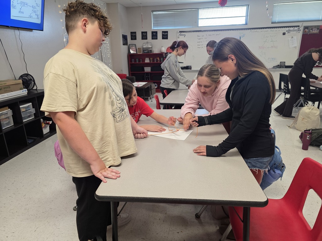 Team building in Mrs. Mulhall's class! Multiple students are working together to draw on a piece of paper with a single writing utensil and string. 