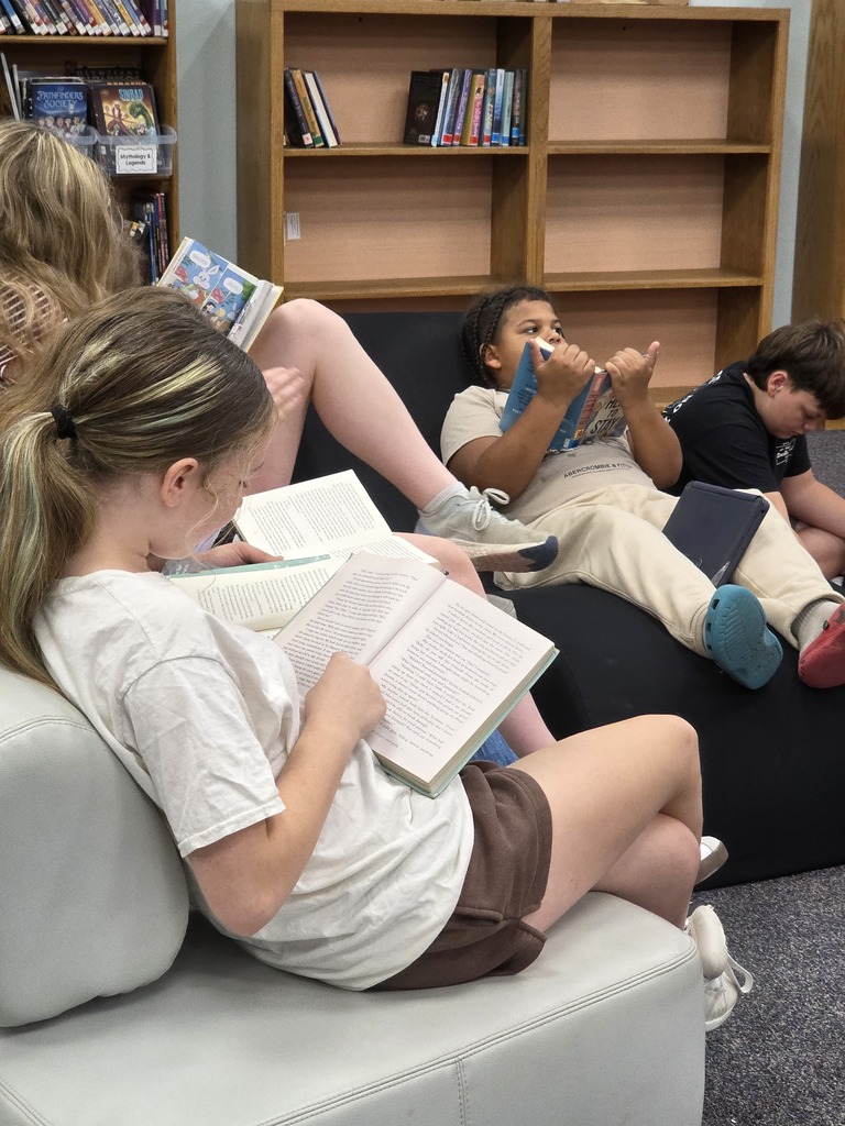 Three people on a couch, reading books. A woman with long blonde hair lies on the couch.