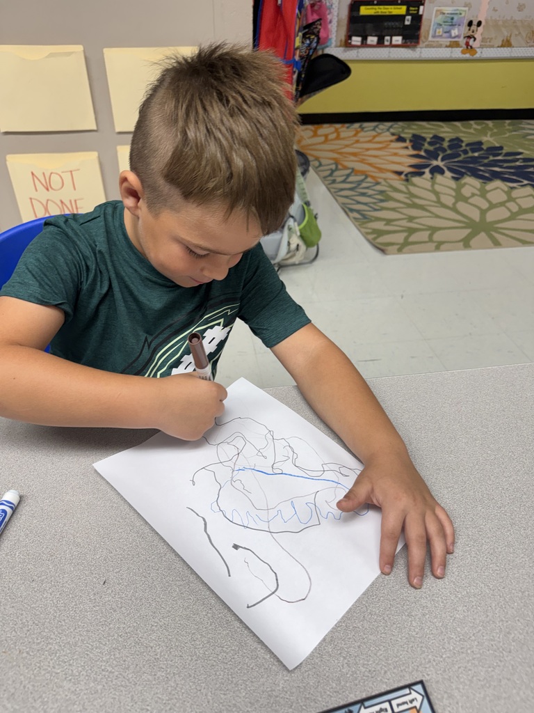 A child wearing a green shirt is seated at a table, coloring with a marker.