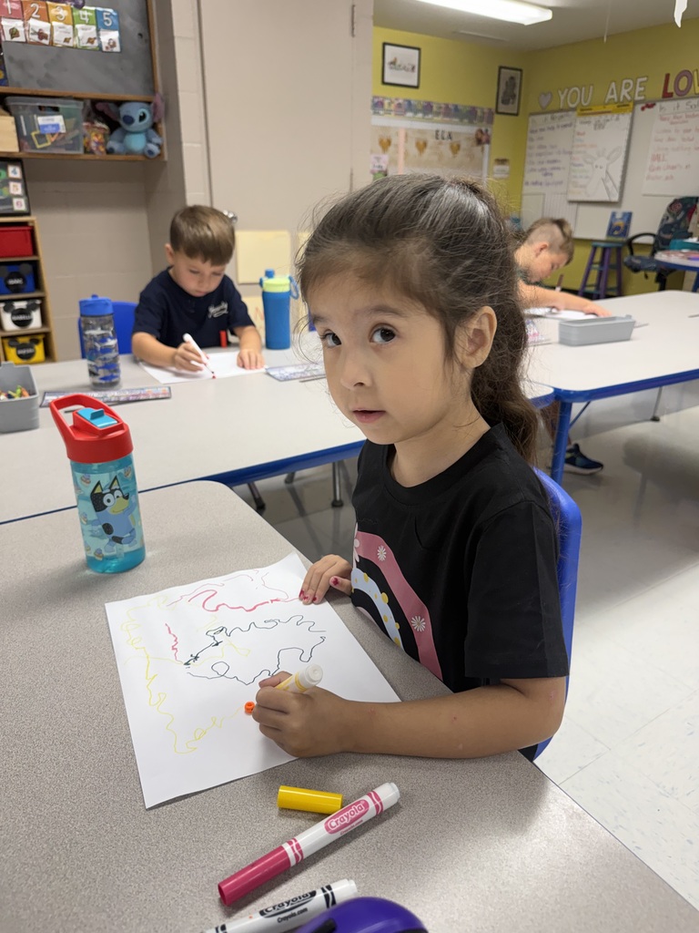 A girl sits at a table, coloring a picture with crayons.