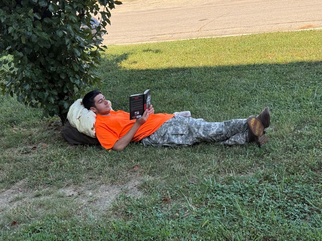 A person lies on grass, reading a book.