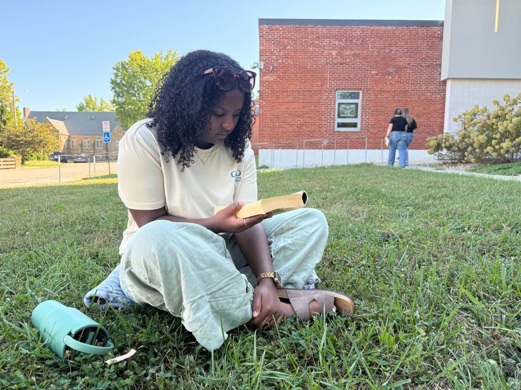 A person sits on grass, reading a book.