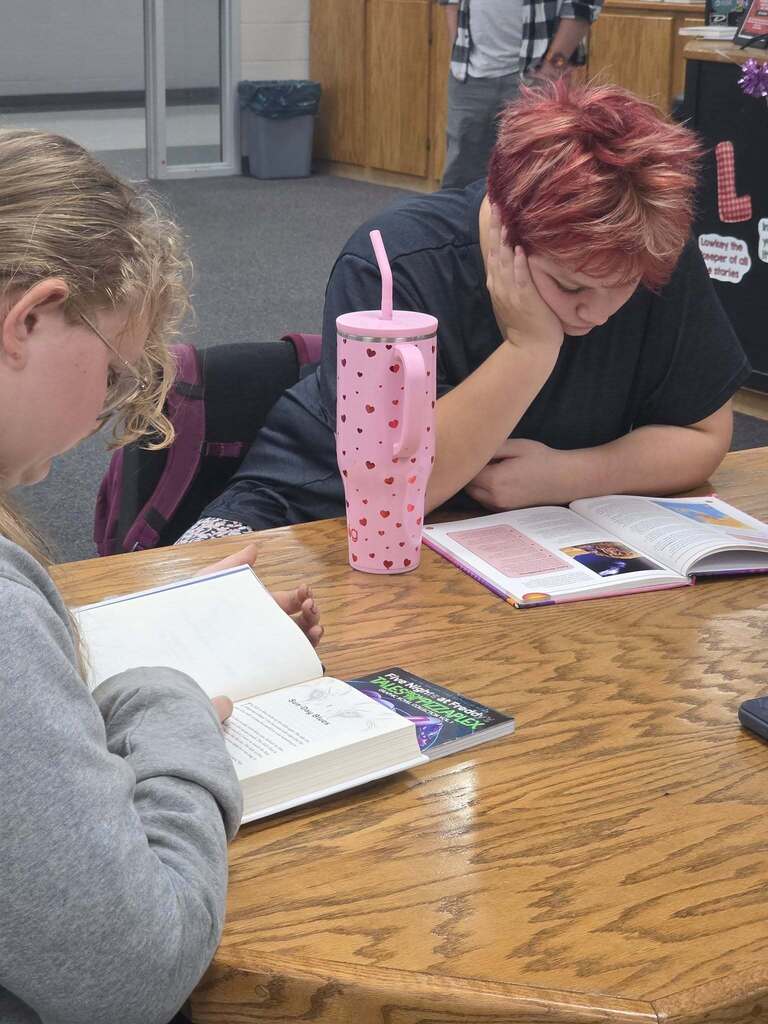 Two students sit at a table reading. 