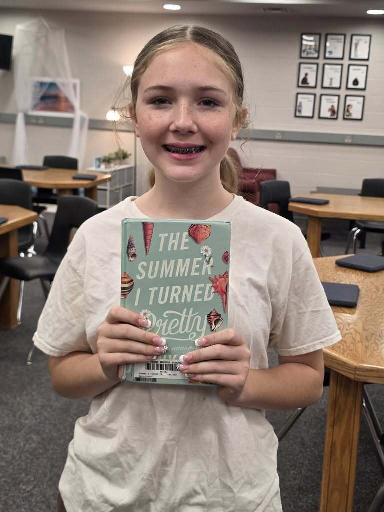 Girl smiling and holding a book titled "The Summer I Turned Pretty". 