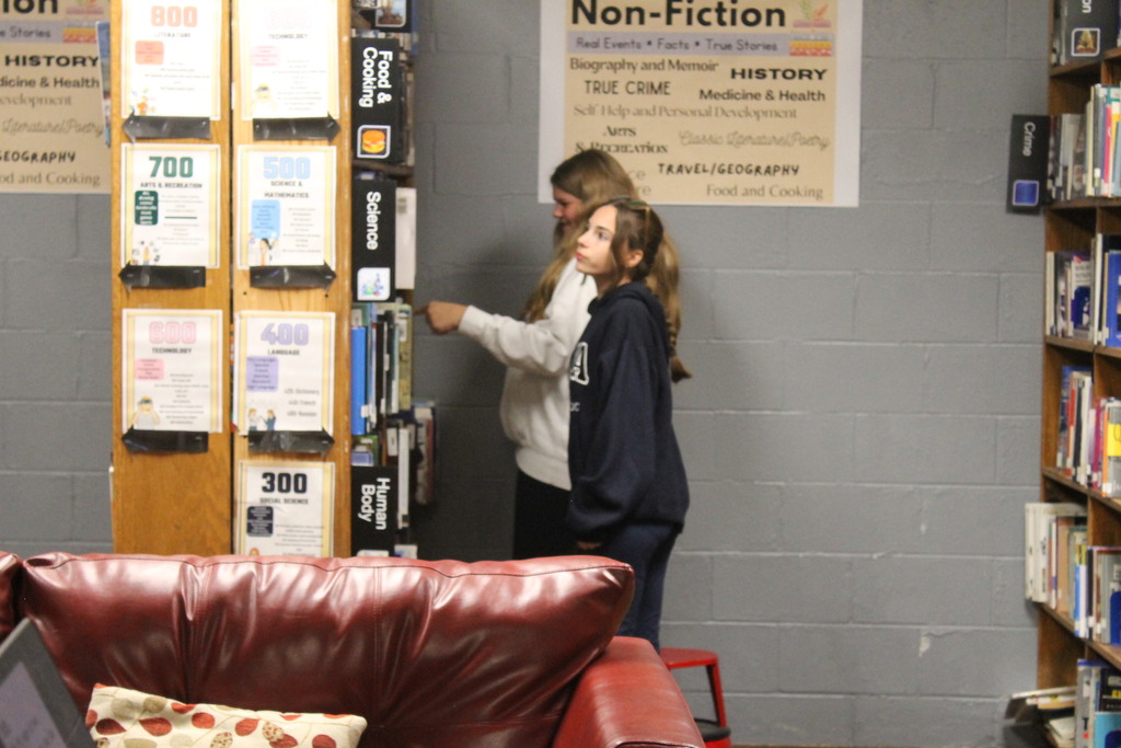 Two people near a book display looking for answers for their scavenger hunt.