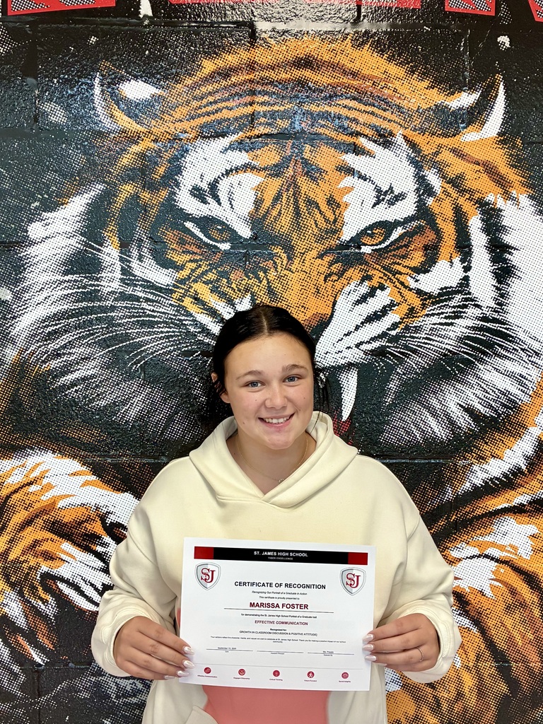 A woman holding a certificate smiles in front of a wall mural of a tiger.