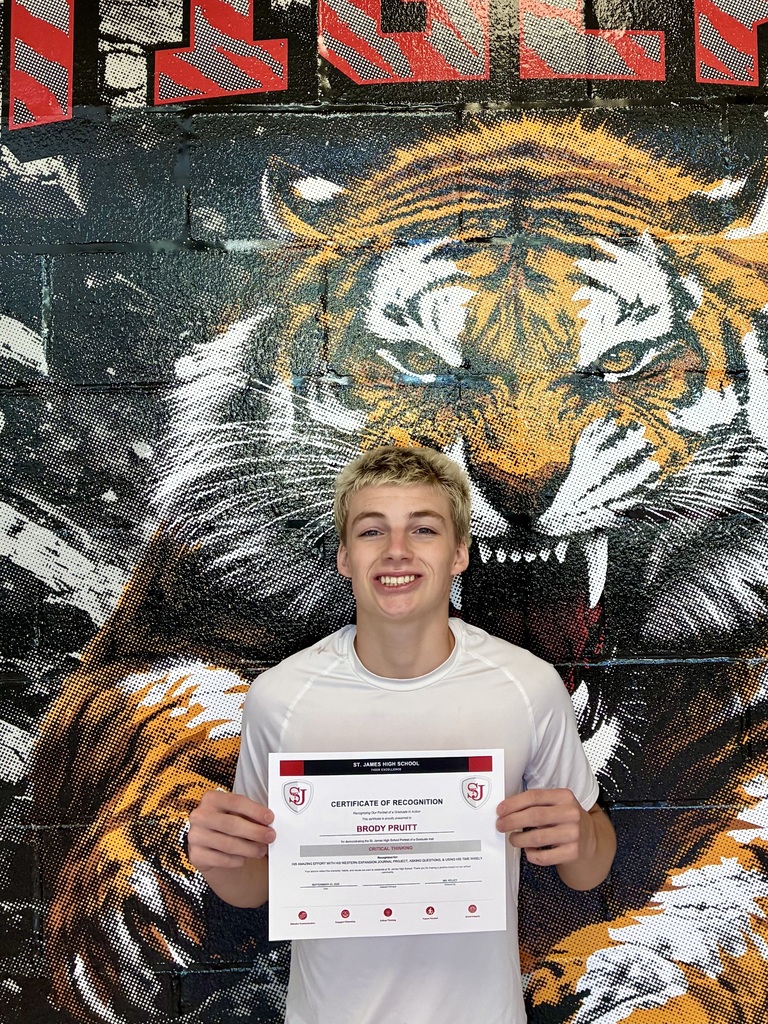 A young man in a white t-shirt holds a certificate in front of a tiger mural.