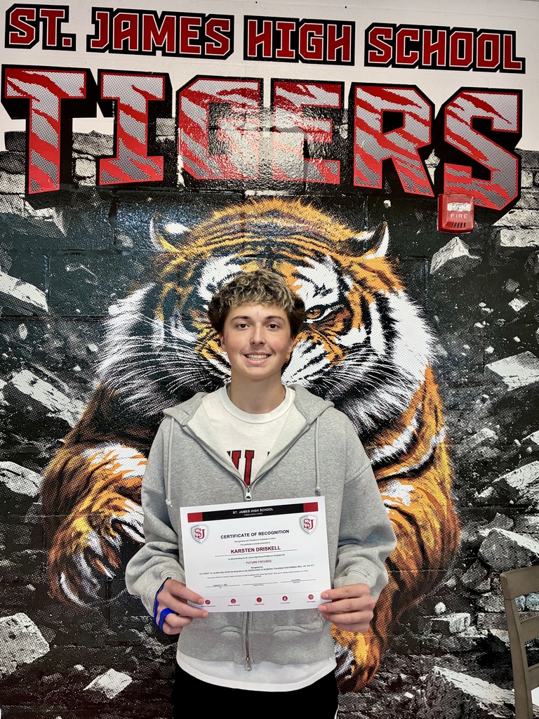 A student holds a certificate in front of a wall with a tiger and "St. James High School Tigers" written on it.