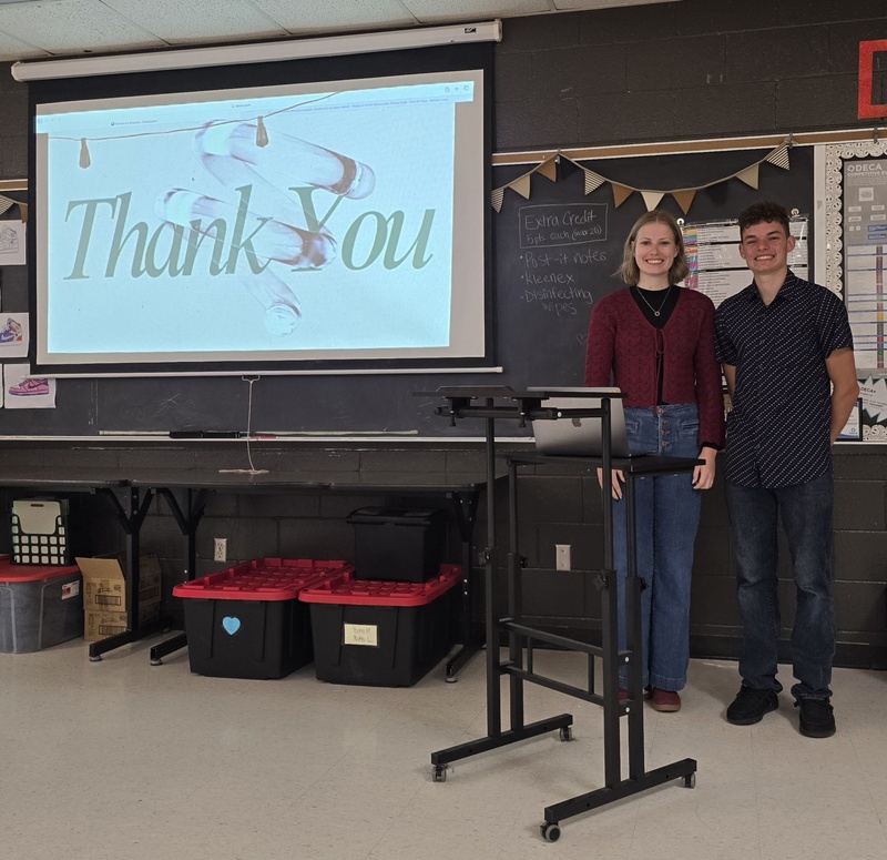 Students stand at front of classroom in front of board to give presentation! 