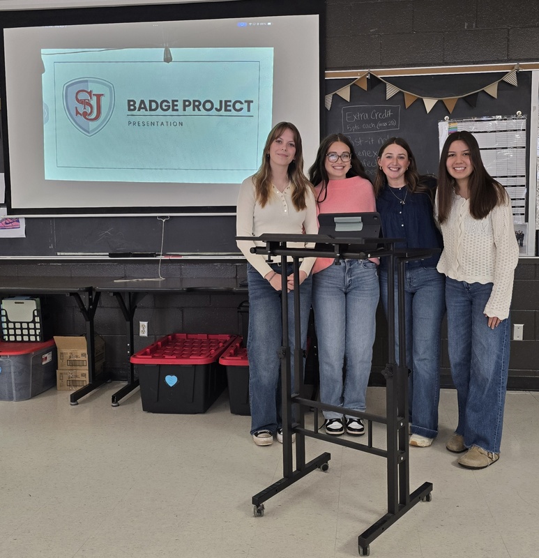 Students stand at front of classroom in front of board to give presentation! 