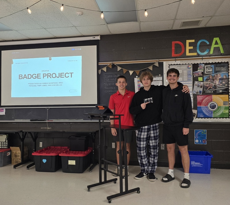 Students stand at front of classroom in front of board to give presentation! 