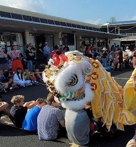 Students sitting around courtyard as the lion walks around and visits with them.