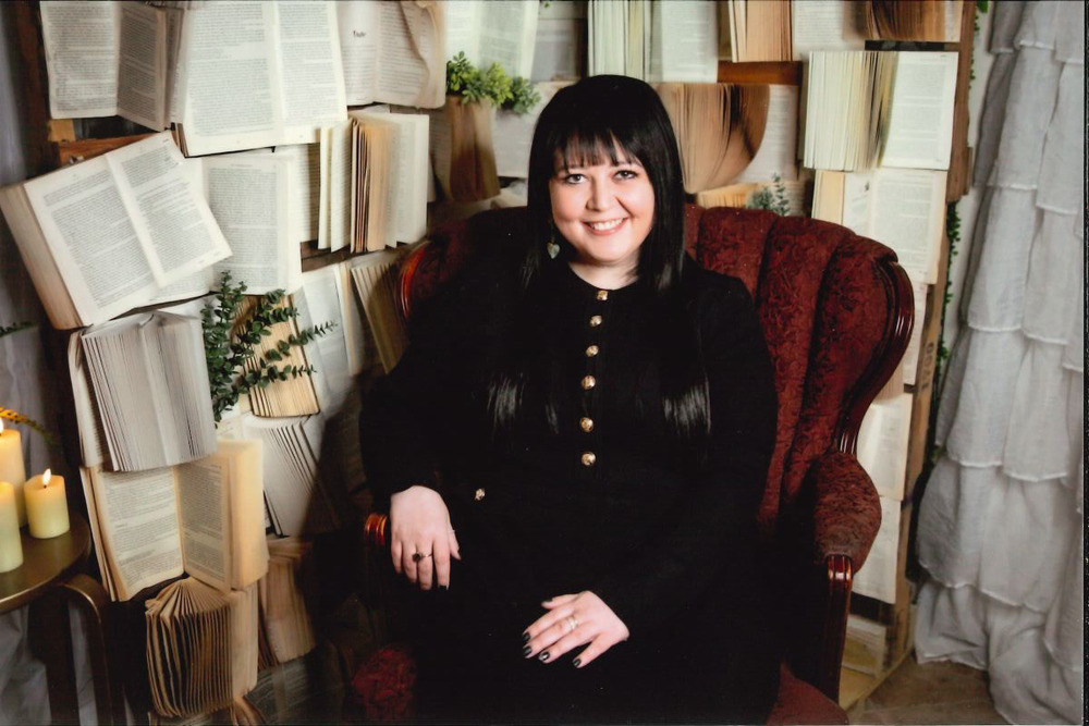 Angela Jackson, a special education teacher at Woodland Developmental Center, sits smiling in a red armchair surrounded by open books arranged as a decorative backdrop.