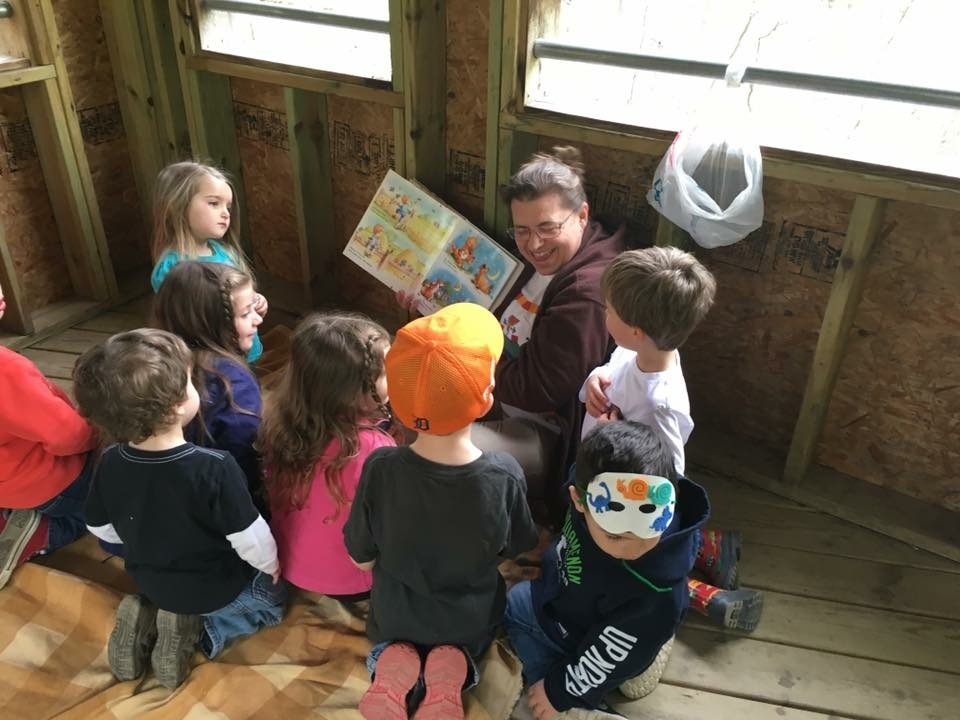 An adult holds a picture book open to a group of seated young children at The Pine River Nature Center during Celebrate Your Child Literacy Day