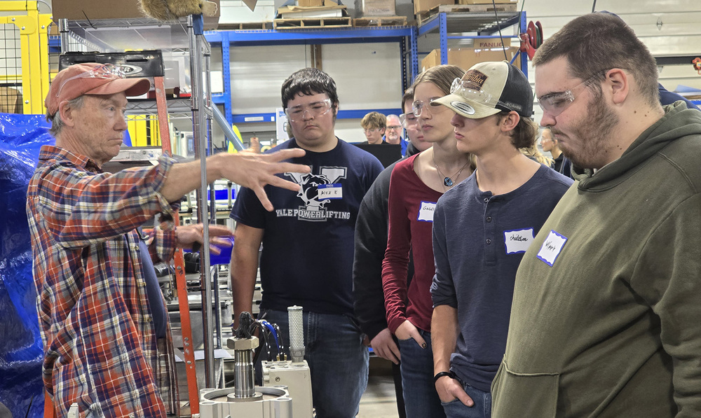 A man gestures to a group of high school students in a manufacturing facility
