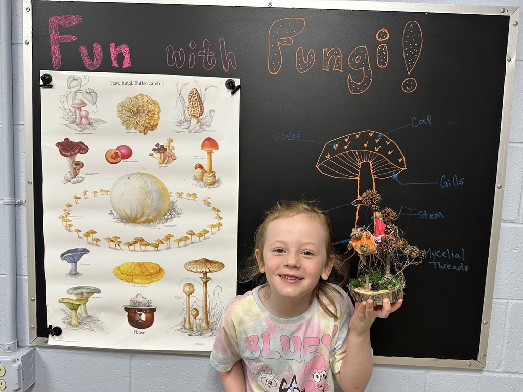 A smiling young girl holds up her fungi creation