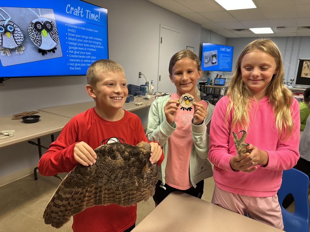 Three students pose with a bird claw, pelt and craft