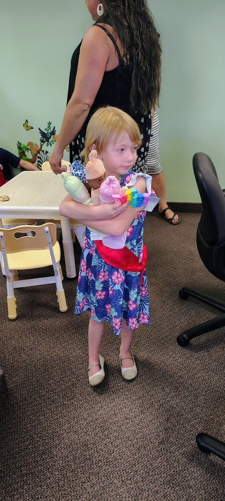 A young child hugs dolls at the new Talking is Teaching space at the Early Childhood Court ribbon cutting