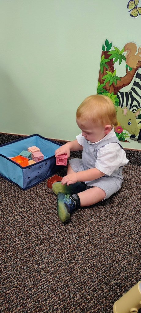 A toddler sits on the floor playing with blocks at the new Talking is Teaching space at the Early Childhood Court ribbon cutting