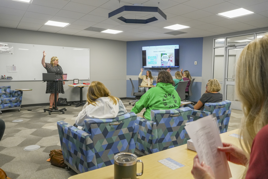A presenter with a raised arm talking to a room of people